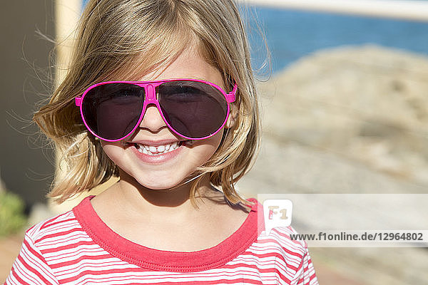 Porträt eines hübschen kleinen lächelnden blonden Mädchens mit Brille von rosa Erwachsenen.