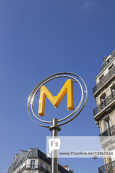 'France Paris department 75 metro signage: yellow ''M'' letter with a blue sky in the background.'