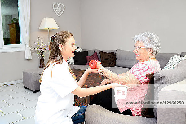 Junge Krankenschwester in der Physiotherapie hilft älteren Frauen bei der körperlichen Rehabilitation zu Hause