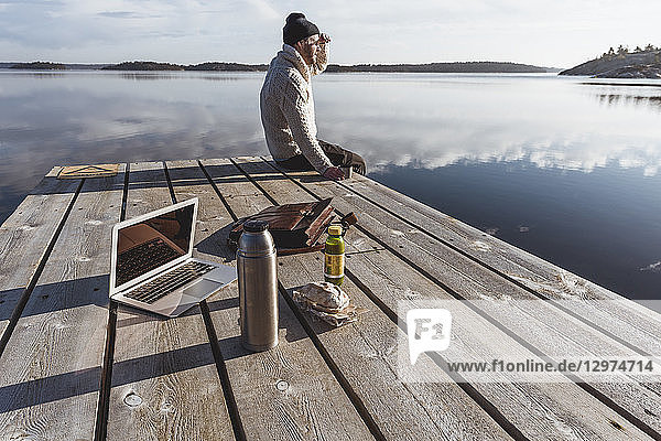 Man on pier next to laptop and lunch in Sodermanland, Sweden