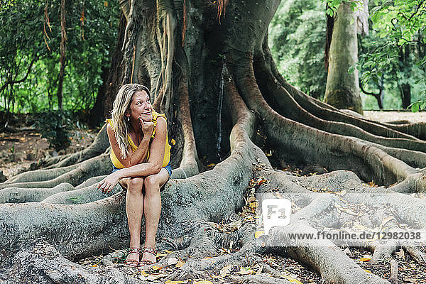 Frau sitzt auf den Wurzeln eines Baumes