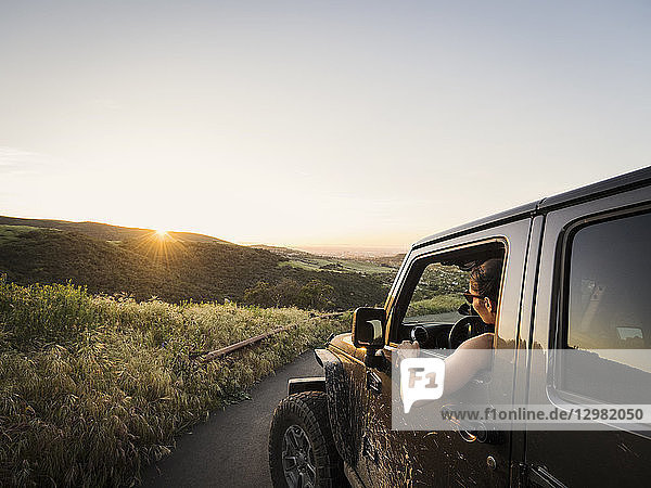 Frau im Geländewagen mit Blick auf den Sonnenuntergang