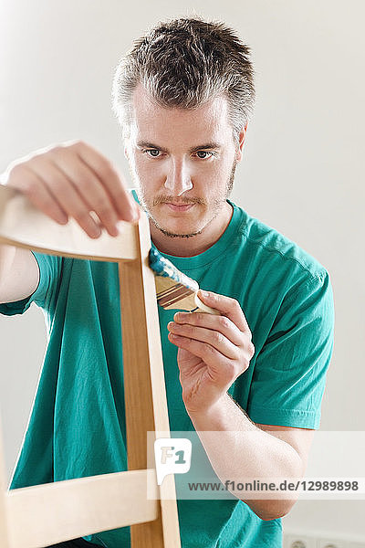 DIY - Mann streicht Holzstuhl mit türkiser Farbe