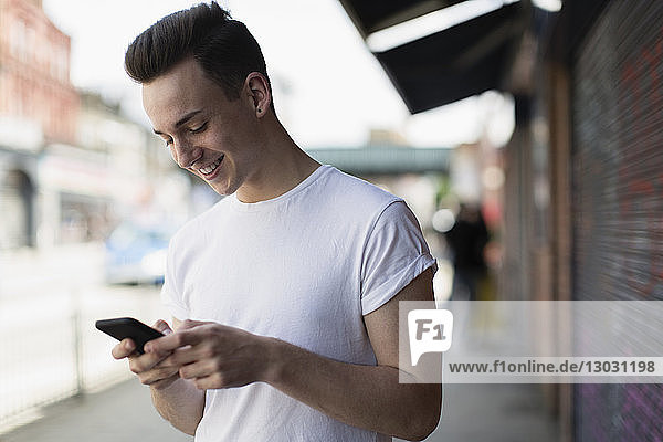 Smiling teenage boy using smart phone on urban sidewalk