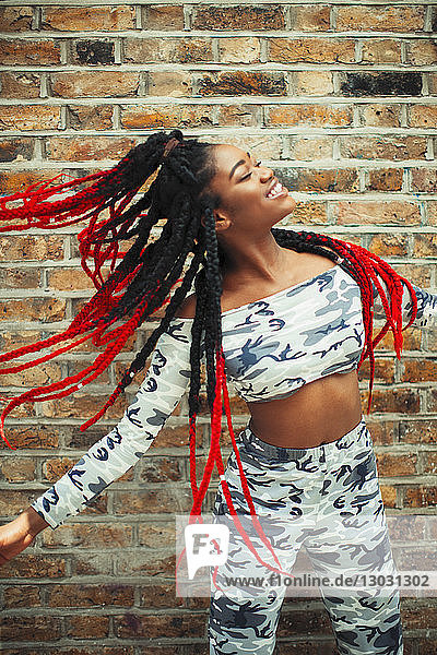 Carefree young woman in camouflage clothing dancing against brick wall