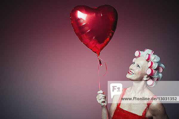 Portrait smiling senior woman with hair in curlers holding heart-shape balloon