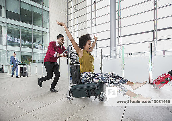 Playful couple running with luggage cart in airport