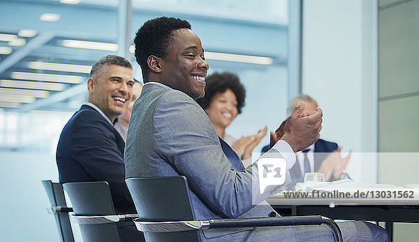 Smiling businessman clapping in conference room meeting