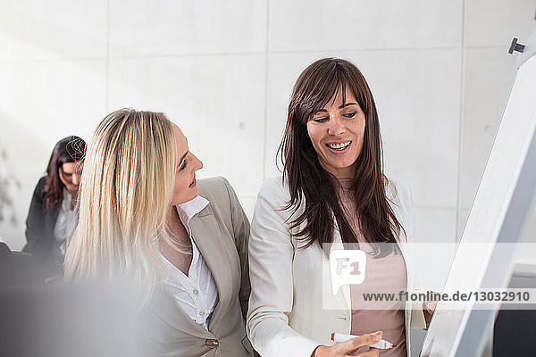 Geschäftsfrauen im Gespräch mit Kollegen und Schreiben an der Tafel im Büro