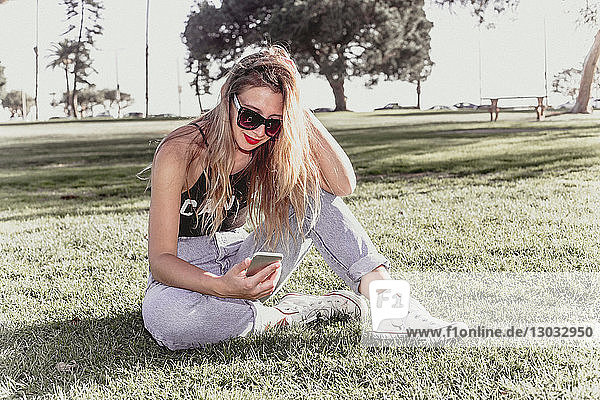 Hippe junge Frau benutzt Mobiltelefon im Park