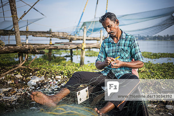 Fischer  der ein Netz flickt  dahinter traditionelle chinesische Fischernetze  Fort Kochi (Cochin)  Kerala  Indien