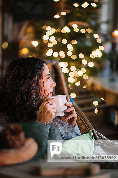 Junge Frau trinkt Kaffee in Café mit dekorativer Beleuchtung