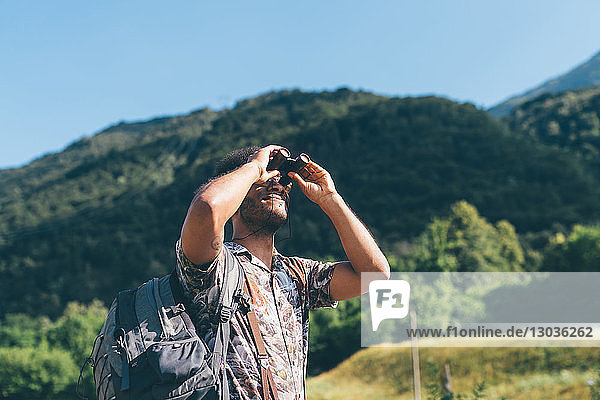 Junger männlicher Wanderer  der durch ein Fernglas nach oben schaut  Primaluna  Trentino-Südtirol  Italien