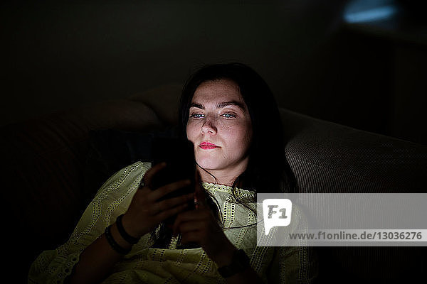 Teenager-Mädchen liegt im Dunkeln auf Sofa und liest SMS
