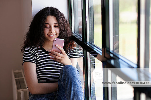 Teenagerin liest Textnachricht auf Handy durch Glasfenster