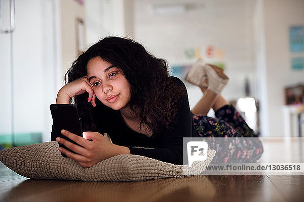 Teenager-Mädchen liegt auf einem Kissen auf dem Boden und liest eine Textnachricht