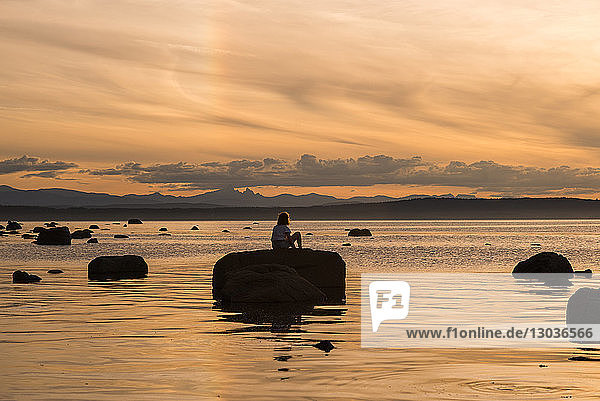 Junge Frau sitzt bei Sonnenuntergang auf einem Felsen  Quadra Island  Campbell River  Kanada