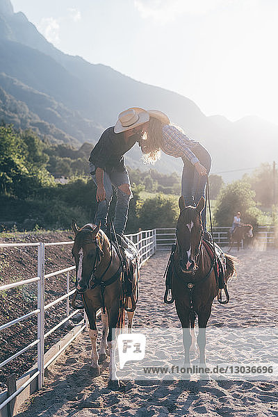 Cowgirl and boyfriend standing on horseback kissing in equestrian arena  Primaluna  Trentino-Alto Adige  Italy