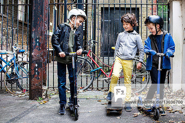 Jungen fahren Roller und Skateboard  Fahrräder im Hintergrund