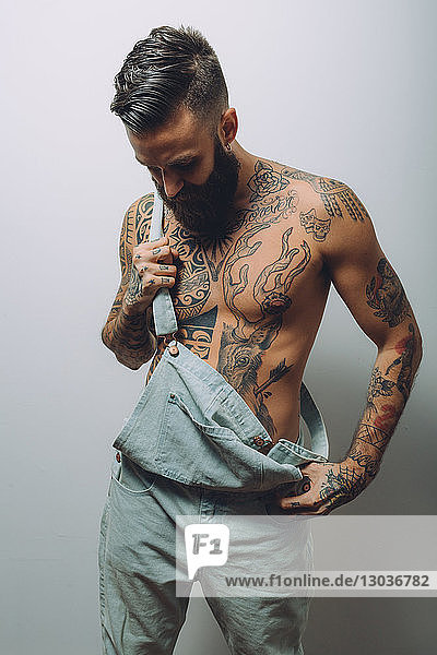Portrait of young man with wearing dungarees  bare chest covered in tattoos