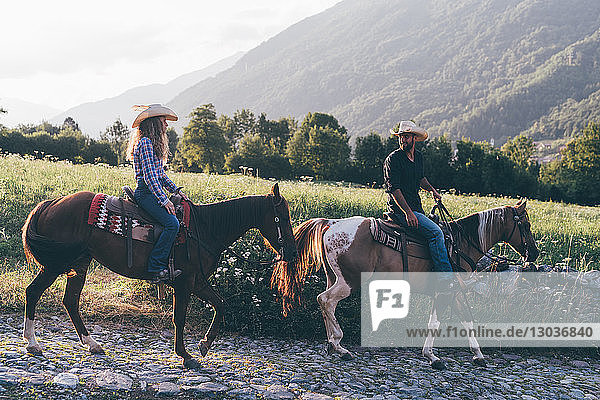 Cowgirl and cowboy riding horses on rural cobbled road  Primaluna  Trentino-Alto Adige  Italy