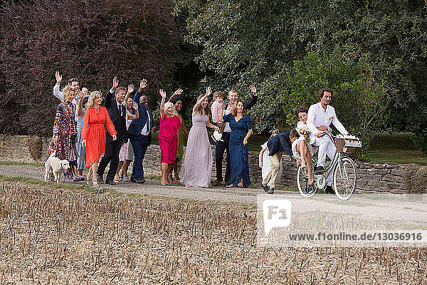 Hochzeitsgäste winken dem Brautpaar auf Fahrrädern