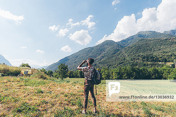 Junger männlicher Wanderer  der durch ein Fernglas in Richtung Berge blickt  Primaluna  Trentino-Südtirol  Italien