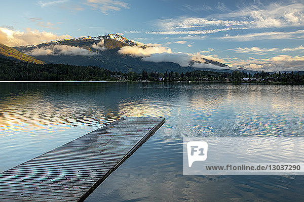 A dock leads into Green Lake  a glacier fed lake  in Whistler. Whistler Blackcomb Ski Resort can be seen in the background catching the last light of the day  British Columbia  Canada
