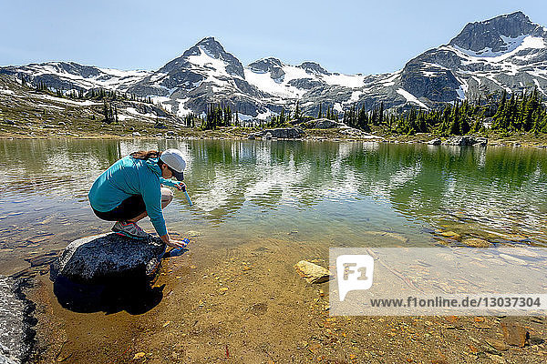 A women fills up a water bottle with a filter from an alpine lake during a hike on a hot summer day in the mountains around Pemberton  British Columbia  Canada