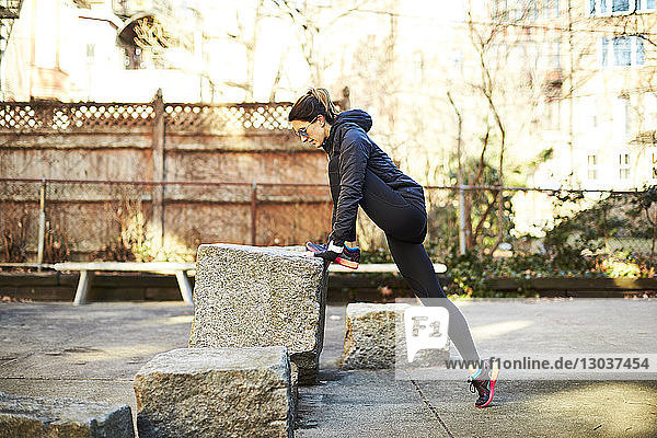 Seitenansicht einer einzelnen mittelgroßen erwachsenen Läuferin  die sich in einem Park in einer Stadt dehnt