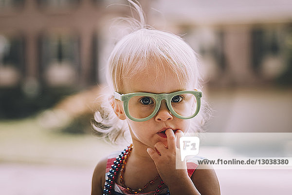 Bildnis eines süßen Mädchens mit Brille und Finger im Mund
