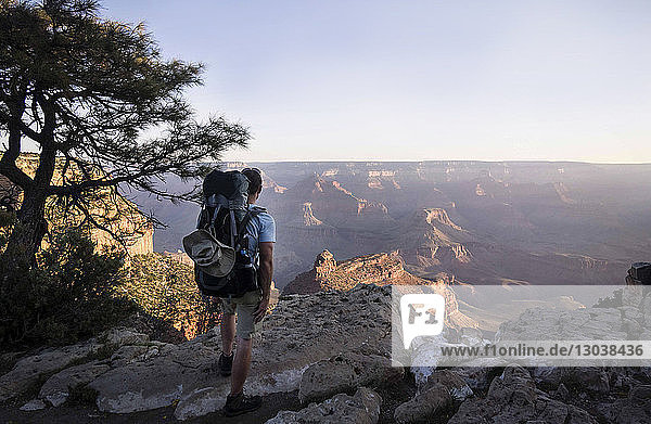 Rear view of man with backpack standing on mountain against at grand canyon