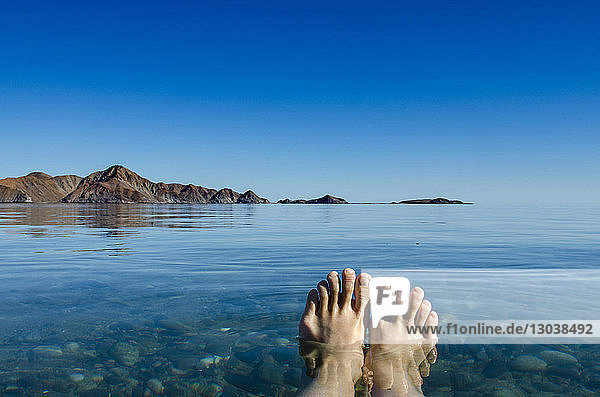 Beschnittenes Bild des Beines eines Mannes im Meer vor klarem blauen Himmel