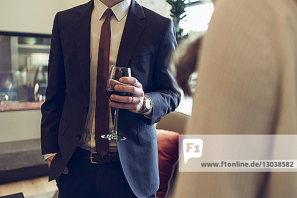 Mittelteil eines Geschäftsmannes  der Weinglas hält  während er mit einem Kollegen im Hotel steht