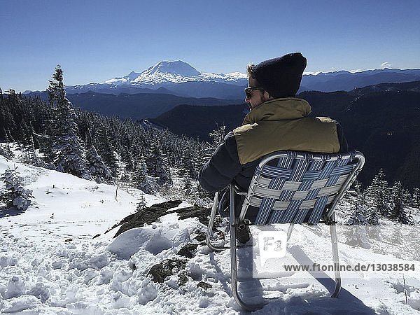 Rear view of man sitting on deck chair in snow covered field