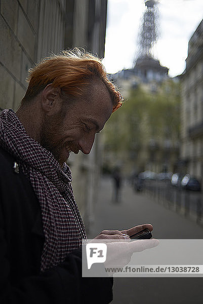Side view of smiling male tourist using smart phone on street with Eiffel Tower in background