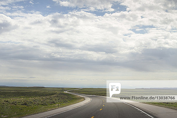 Country road amidst field against cloudy sky at Yellowstone National Park