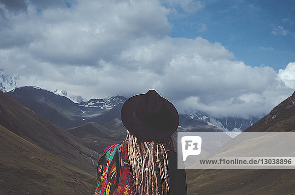Rückansicht einer Frau mit Hut  die auf einer Landschaft vor bewölktem Himmel steht