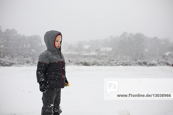 Boy wearing warm clothing while standing on snowy field during snowfall
