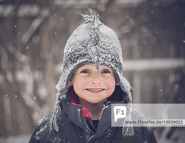 Porträt eines fröhlichen Jungen mit Hut bei Schneefall