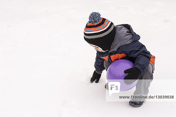 Hochwinkelaufnahme eines Jungen mit Ball  der auf einem schneebedeckten Feld spielt