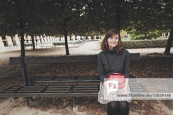 Lächelnde Frau mit Geldbörse schaut weg  während sie im Park auf einer Bank sitzt