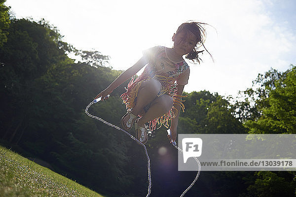 Niedrigwinkelansicht eines Mädchens  das im Sommer im Park gegen den Himmel springt