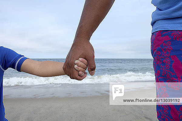 Ausgeschnittenes Bild von Vater und Sohn  die sich am Strand am Meer an den Händen halten