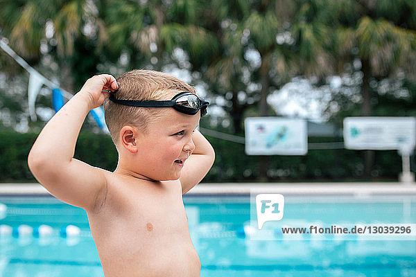 Side view of boy wearing swimming goggles while standing by pool