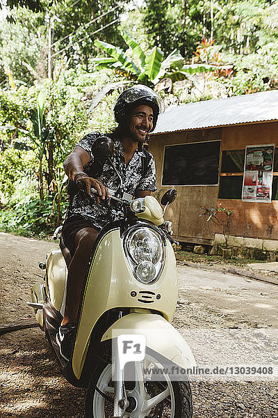 Cheerful man wearing helmet while driving motor scooter on dirt road