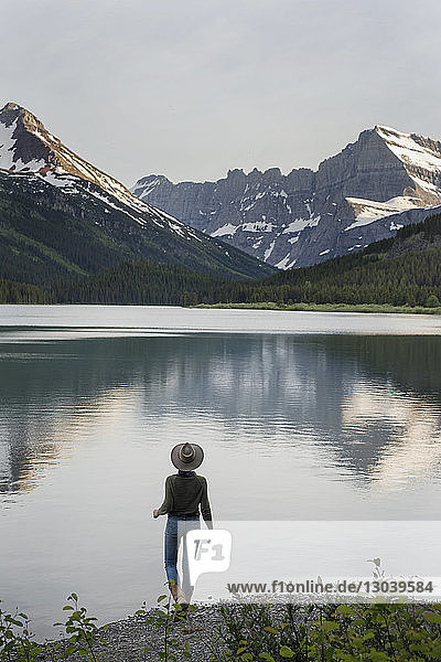 Rückansicht einer Wanderin  die am Ufer des Swiftcurrent Lake stehend auf den Mt. Grinnell blickt