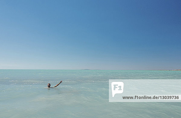 Man swimming in sea against clear sky on sunny day