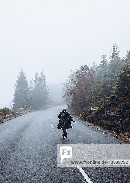Rear view of woman running on road against sky during foggy weather