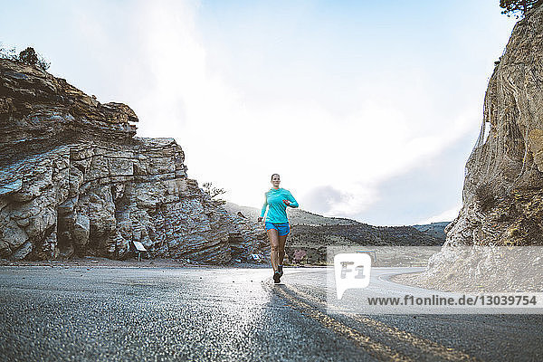 Sportlerin rennt auf Landstrasse inmitten von Bergen gegen den Himmel